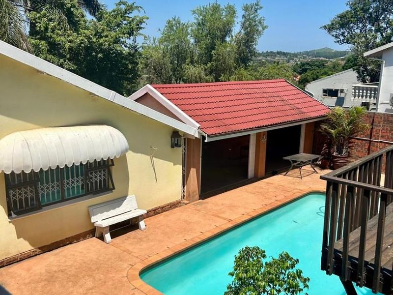 Outdoor pool area featuring a swimming pool, terracotta paving, and a covered structure with a red tiled roof, set within a private garden.