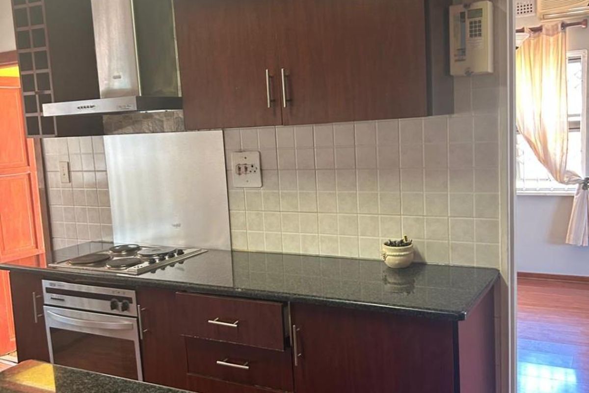 A functional kitchen featuring dark wood cabinetry, granite countertops, a built-in oven and hob, and a tiled backsplash.