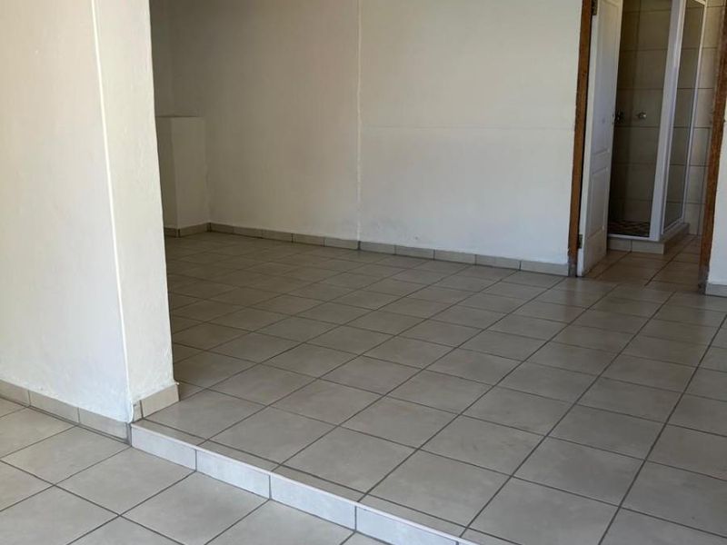 An empty living area featuring tiled flooring, a raised floor section, and direct access to an adjacent bathroom.