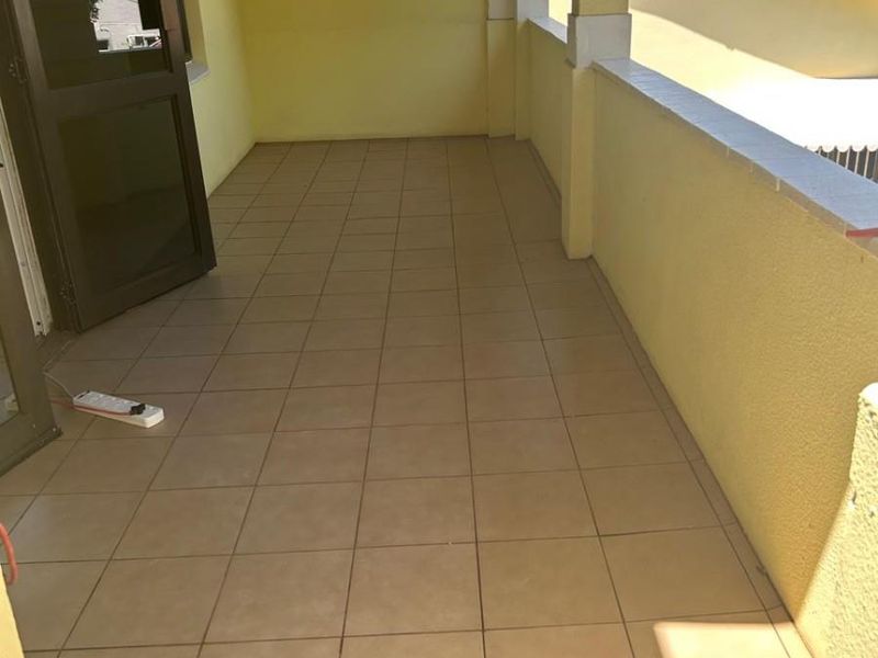 A covered balcony featuring tiled flooring, masonry pillars, and a low parapet wall, offering an open outdoor space.