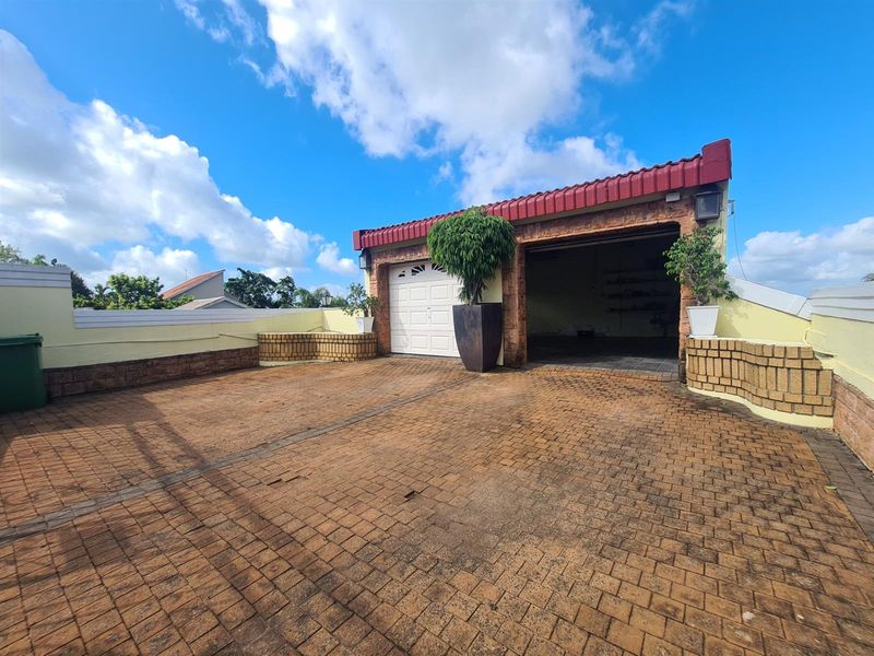 Exterior view of a garage with a paved driveway and brick retaining walls under a tiled roof.