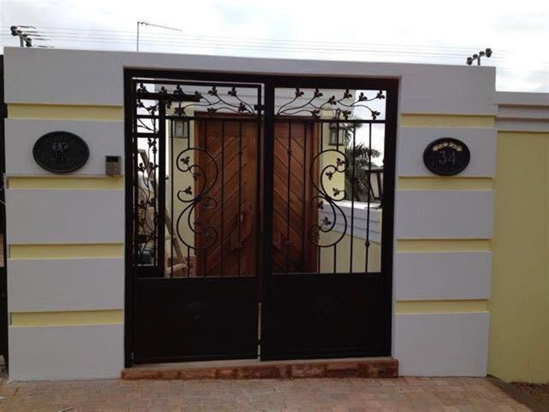 Front entrance featuring a decorative wrought iron gate set within a rendered boundary wall, leading to a solid timber front door.