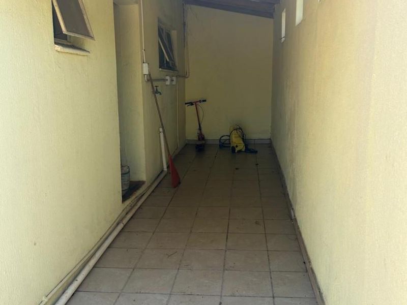 A narrow, covered utility or service passage featuring tiled flooring and exposed timber rafters, suitable for storage or laundry utility purposes.