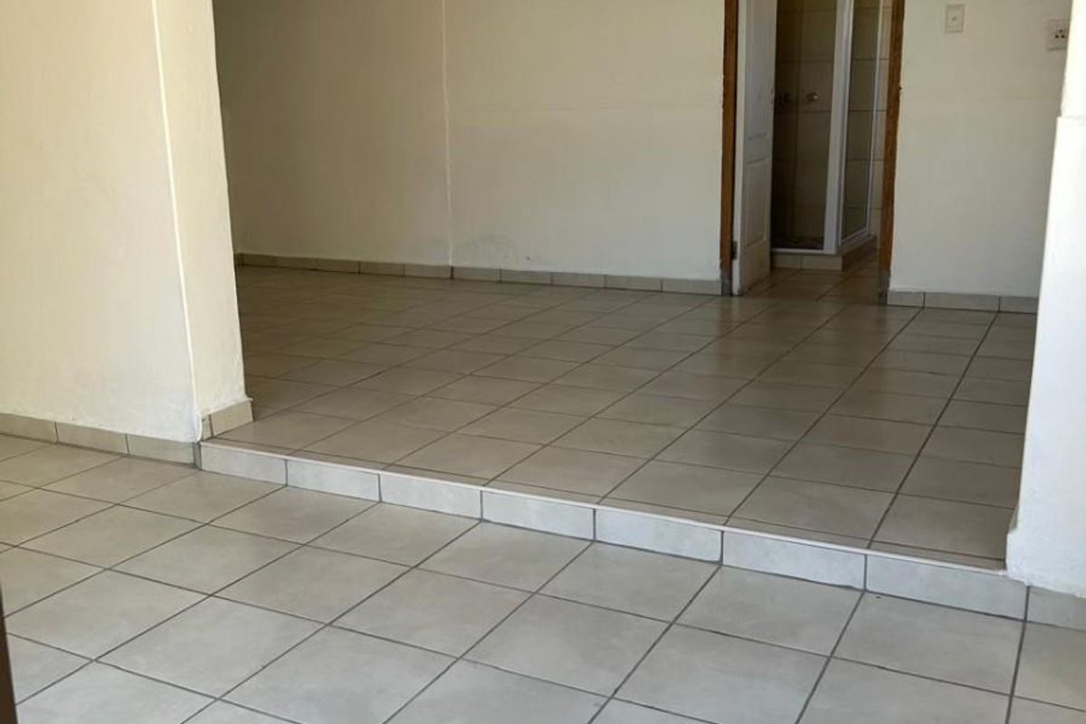 An empty, open-plan living area featuring neutral tiled flooring, a raised floor section, and direct access to an adjacent bathroom.