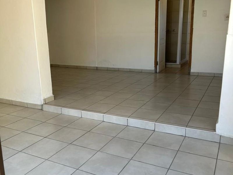 An empty, open-plan living area featuring neutral tiled flooring, a raised floor section, and direct access to an adjacent bathroom.