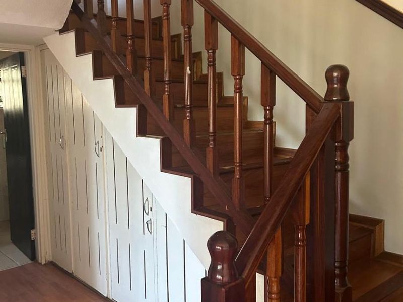 A hallway featuring a traditional wooden staircase with a balustrade and integrated under-stair storage cupboards, finished with laminate flooring.