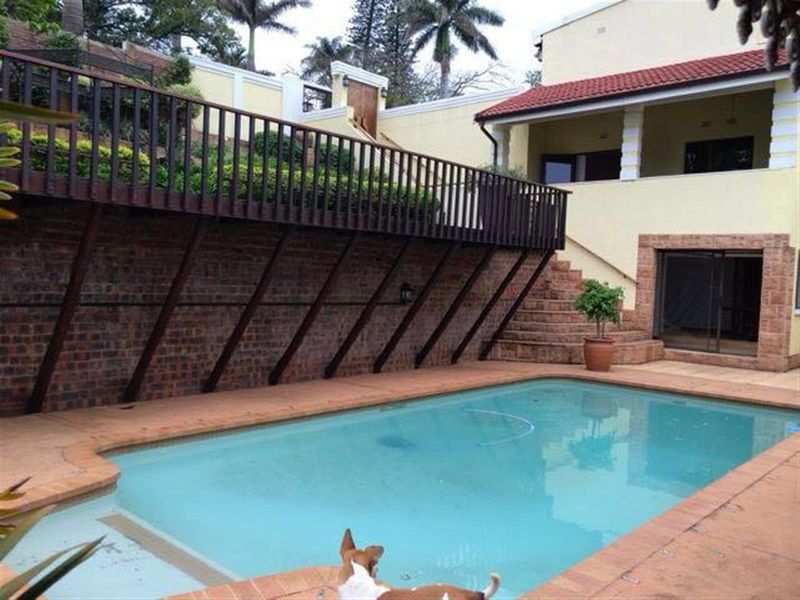 Outdoor pool area featuring a raised wooden deck, brick retaining wall, and tiled pool surround, providing a functional space for outdoor recreation.