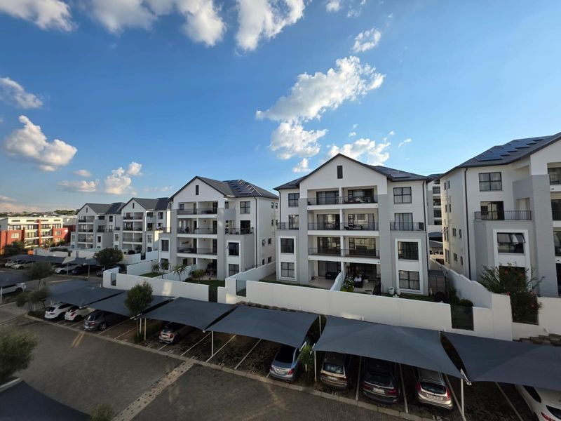 An elevated view of a modern apartment complex featuring multi-story buildings with balconies, solar panels, and covered parking bays.