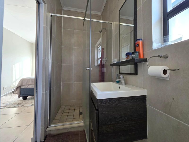 A modern bathroom featuring a glass-enclosed shower, a dark wood-finish wall-mounted vanity with a basin, and neutral wall tiling.