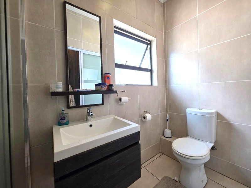 A clean and functional bathroom featuring neutral wall tiles, a modern vanity with basin, and a standard toilet.
