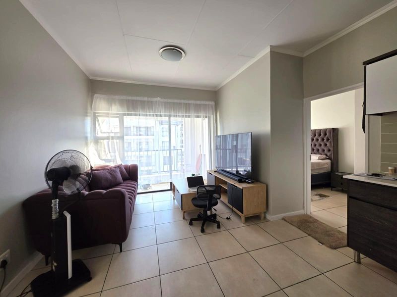 Open plan living area featuring tiled flooring and a sliding glass door providing access to a balcony, with an adjacent view into the bedroom.