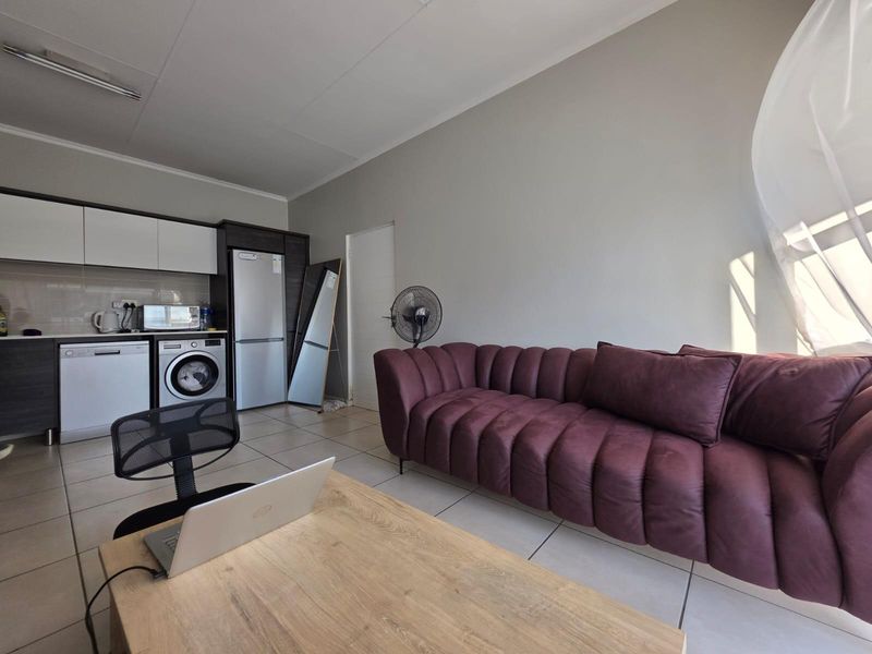 Open plan living area featuring a modern kitchen with built-in cabinetry and integrated laundry appliances, finished with neutral tiled flooring.