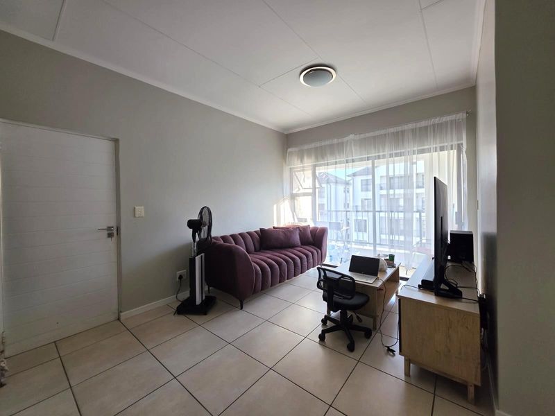A living room featuring tiled flooring and a large sliding glass door providing access to a balcony, with neutral wall finishes.