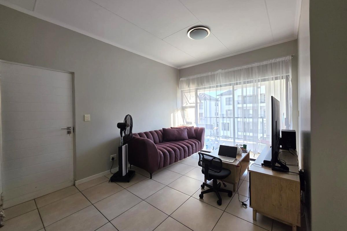 A living room featuring tiled flooring and a large sliding glass door providing access to a balcony, with neutral wall finishes.