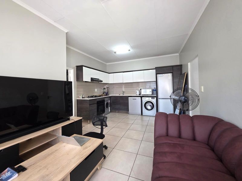 Open-plan living area featuring a modern kitchen with built-in cabinetry, tiled flooring, and integrated appliances, seamlessly connected to the lounge space.