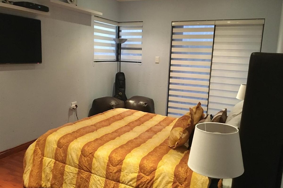 A bedroom featuring laminate flooring, dual-aspect windows with fitted zebra blinds, and a sliding door providing access to the exterior.