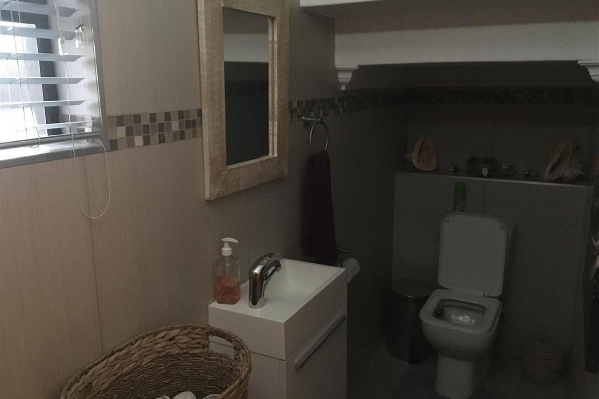 A compact guest bathroom featuring a modern wall-mounted vanity, a toilet, and tiled wall accents with a window for natural light.