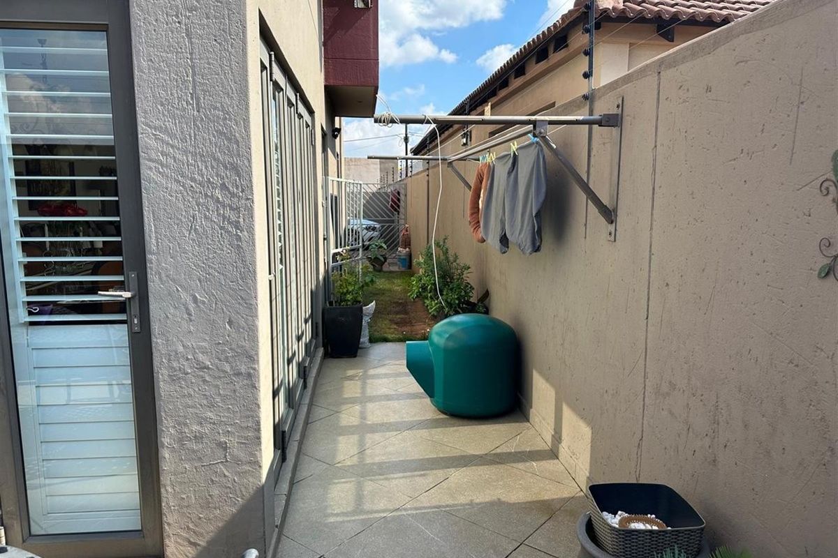 A narrow side courtyard featuring tiled flooring, a wall-mounted drying rack, and perimeter boundary walls with security fencing.
