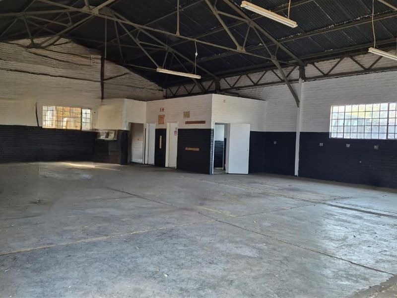 Spacious industrial warehouse or commercial workshop featuring high ceilings, exposed steel trusses, concrete flooring, and multiple access points.
