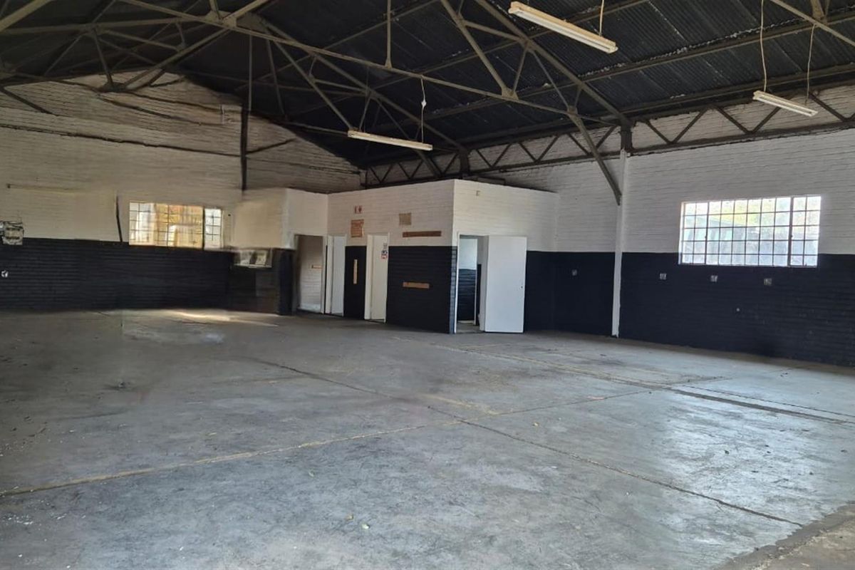 Spacious industrial warehouse or commercial workshop featuring high ceilings, exposed steel trusses, concrete flooring, and multiple access points.