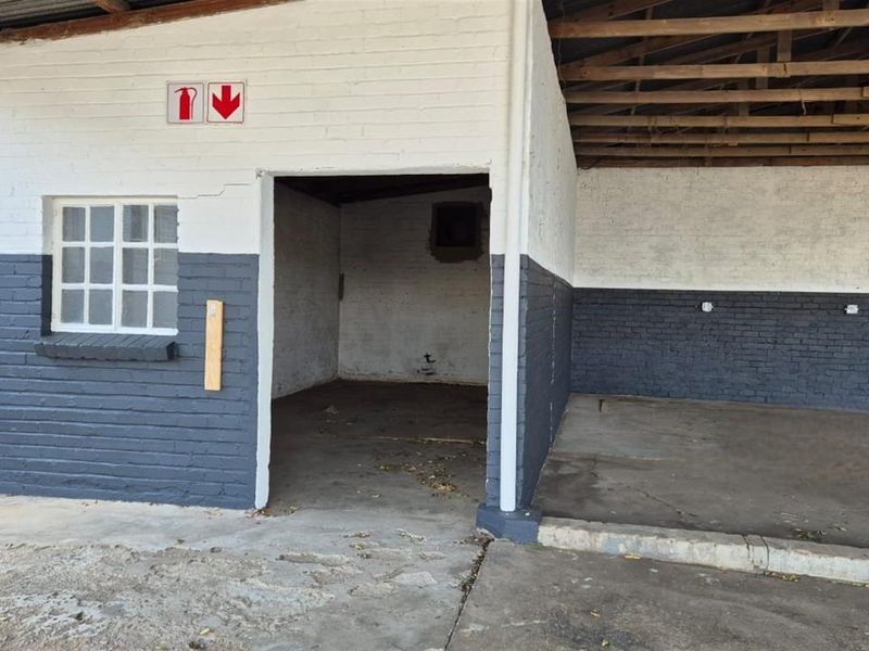 A functional commercial utility space or garage area featuring painted brick walls, concrete flooring, and an open-truss roof structure.