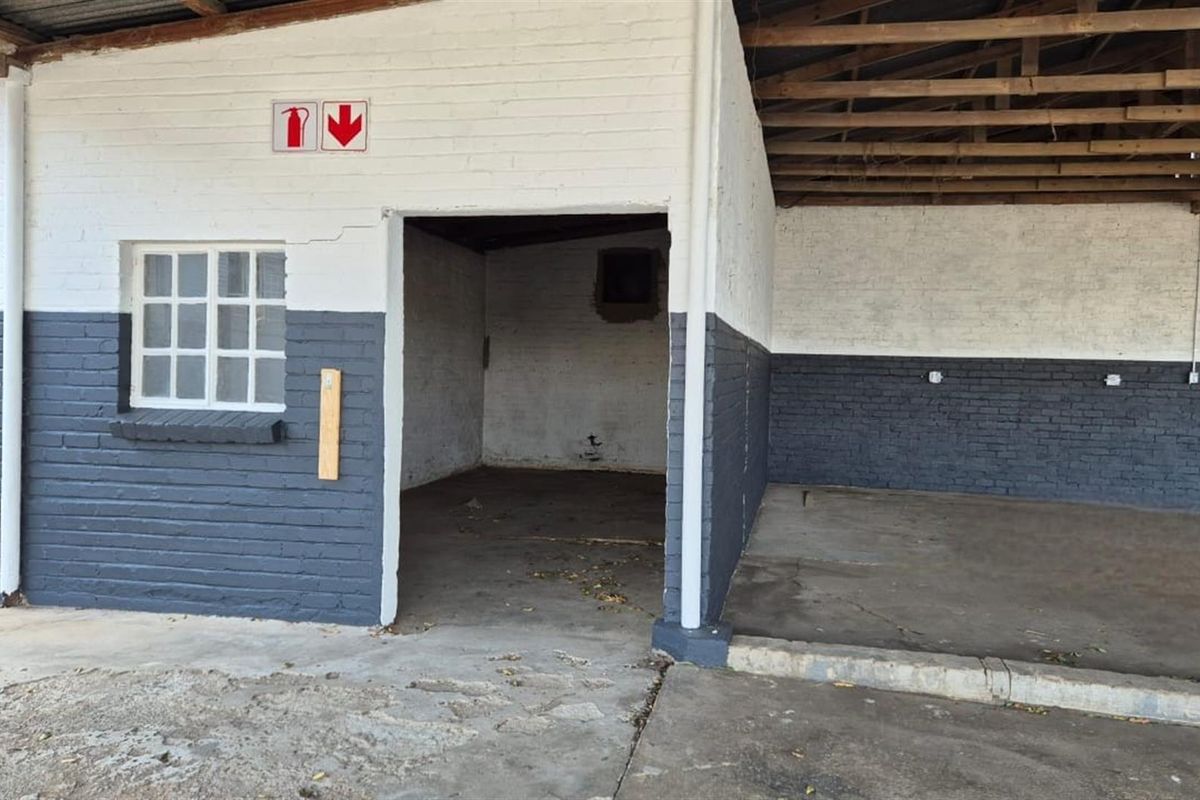 A functional commercial utility space or garage area featuring painted brick walls, concrete flooring, and an open-truss roof structure.