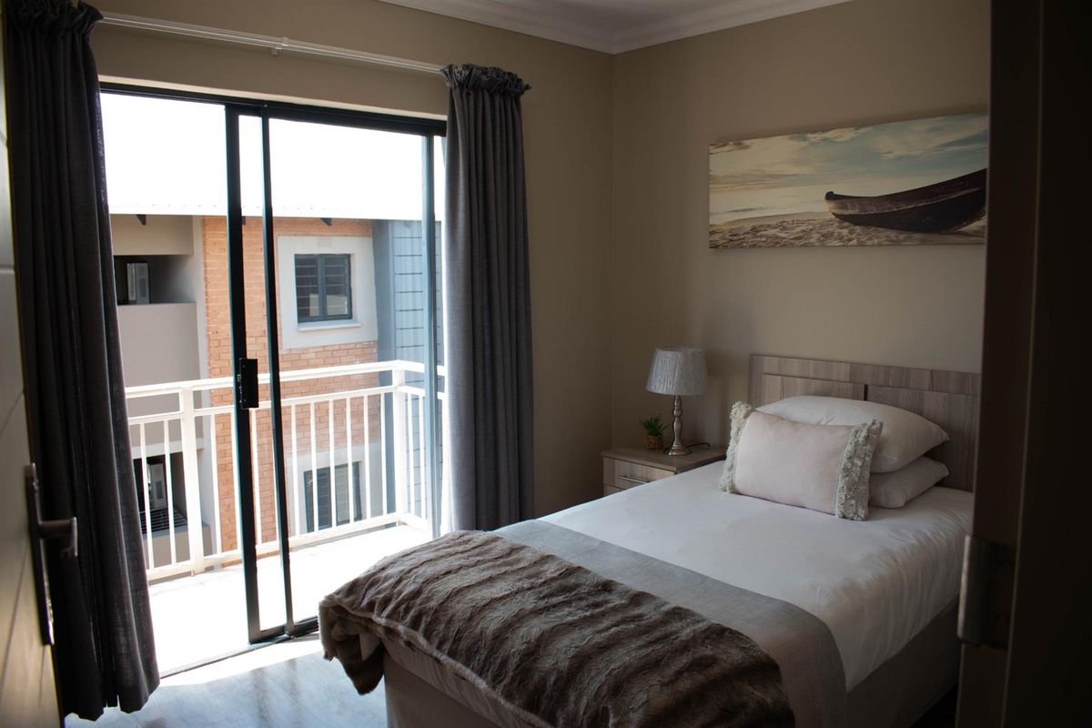 A well-maintained bedroom featuring neutral tones, laminate flooring, and a sliding glass door providing direct access to a private balcony.