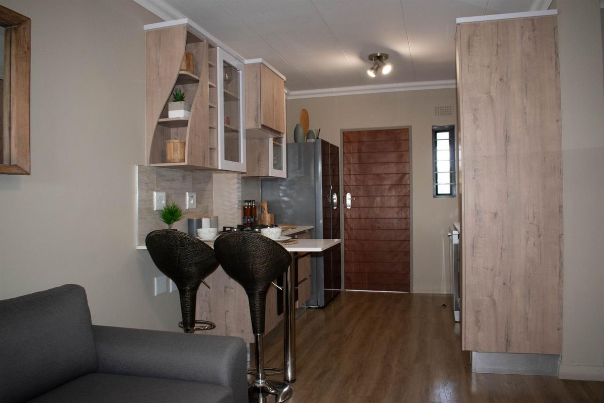 Compact open-plan kitchen featuring light wood-grain cabinetry, a breakfast bar, and integrated storage, seamlessly connecting to the living area.
