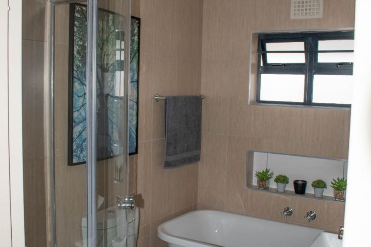 A compact, modern bathroom featuring a glass-enclosed shower, a freestanding bathtub, a wall-mounted basin, and neutral wall tiling.