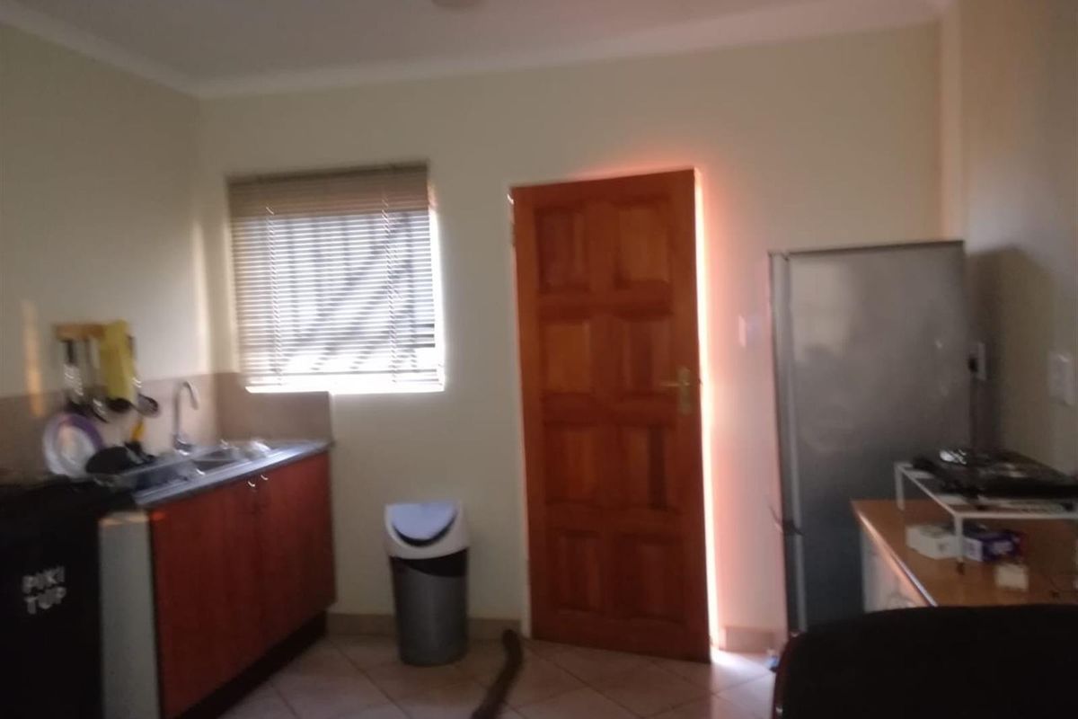 A functional kitchen area featuring wooden cabinetry, a stainless steel sink, tiled flooring, and a window with fitted blinds.
