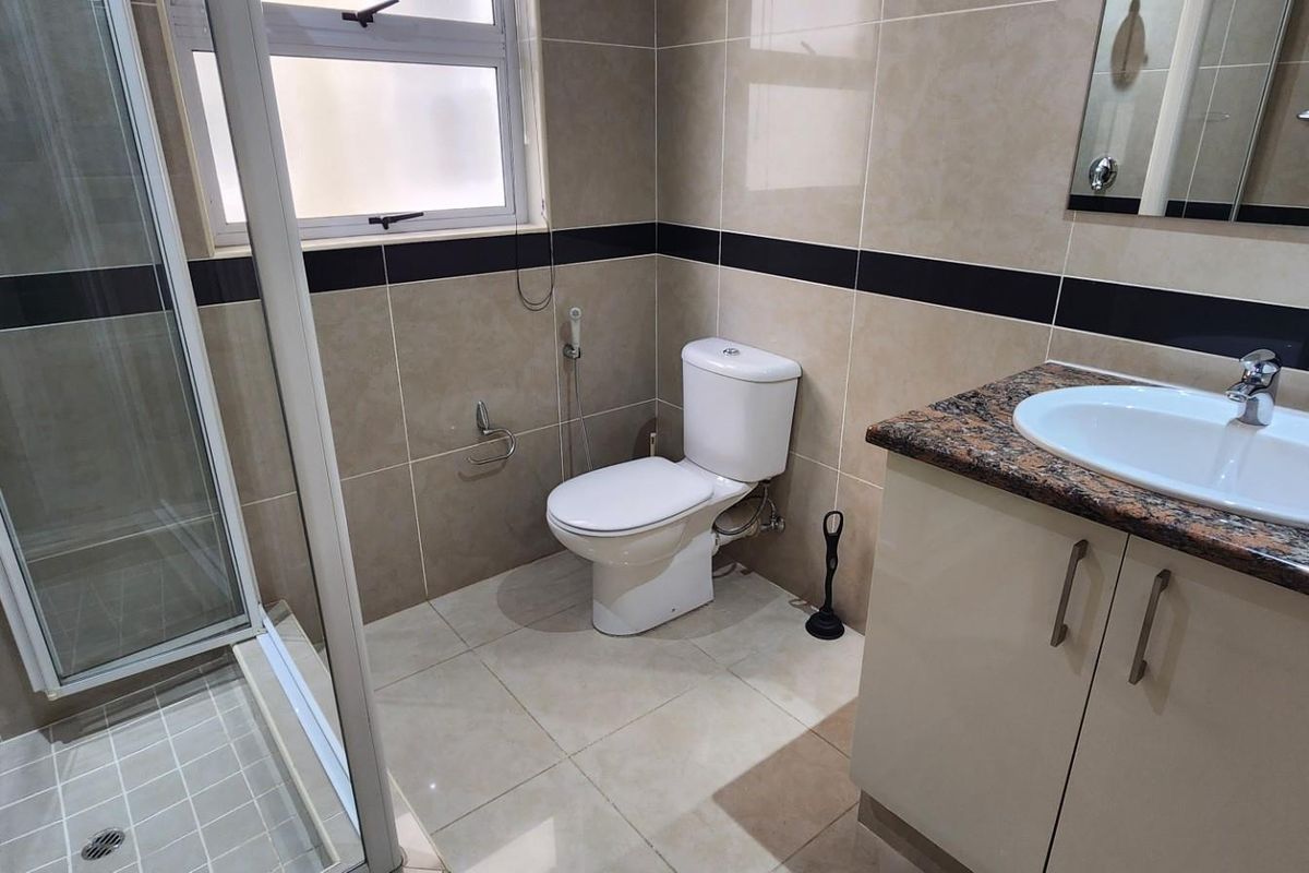 A modern bathroom featuring a glass-enclosed shower, a vanity with a granite countertop, and neutral wall tiling with a decorative black accent border.