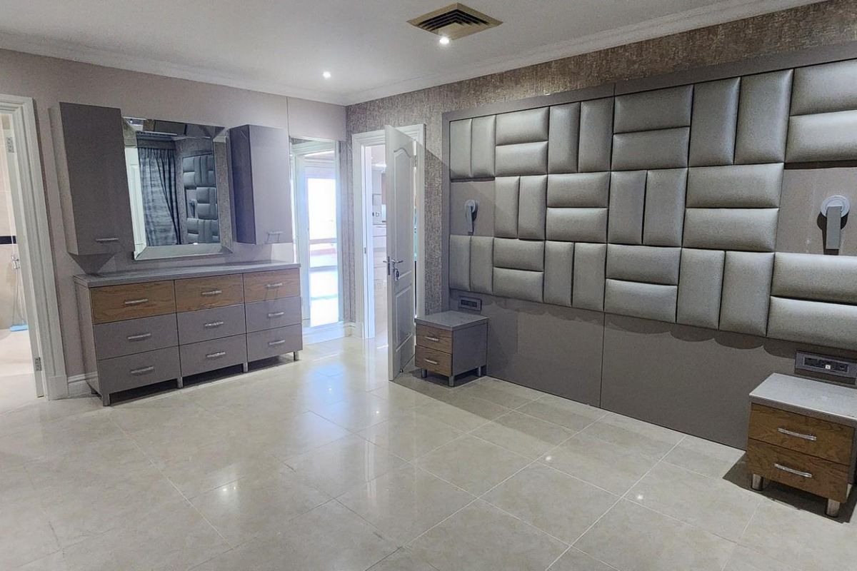 Spacious bedroom featuring a large upholstered feature wall, built-in cabinetry, and direct access to an en-suite bathroom with tiled flooring throughout.