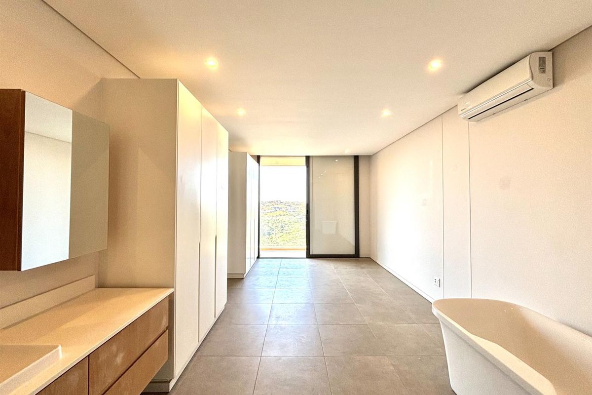 Modern, spacious bathroom featuring a sleek vanity, built-in cabinetry, a freestanding bathtub, and direct access to a private balcony with scenic views.
