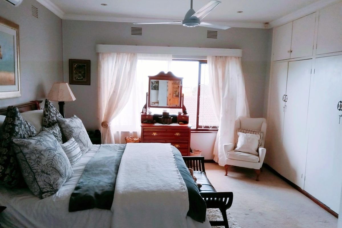 A well-maintained bedroom featuring built-in cupboards, a ceiling fan, and an air conditioning unit, offering a comfortable and functional living space.