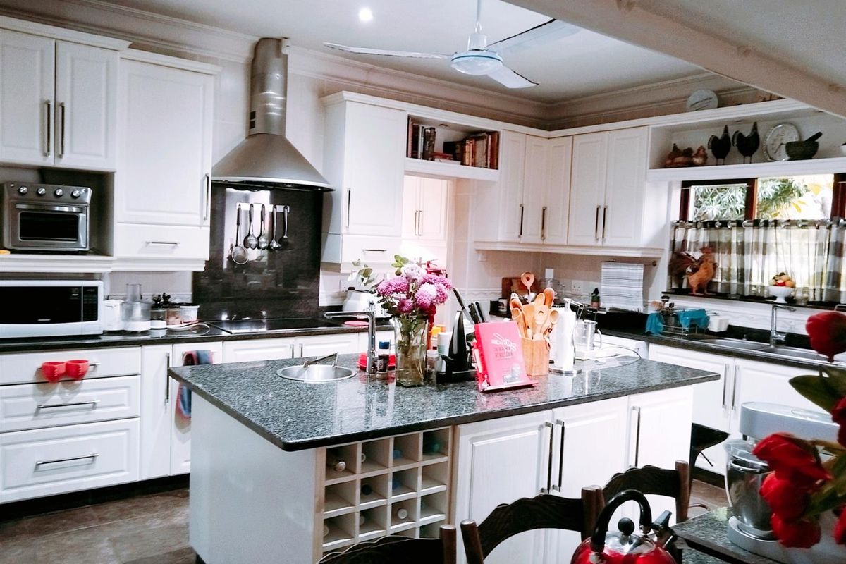 A well-appointed kitchen featuring a central island with granite countertops, ample cabinetry, a stainless steel extractor fan, and integrated appliances.