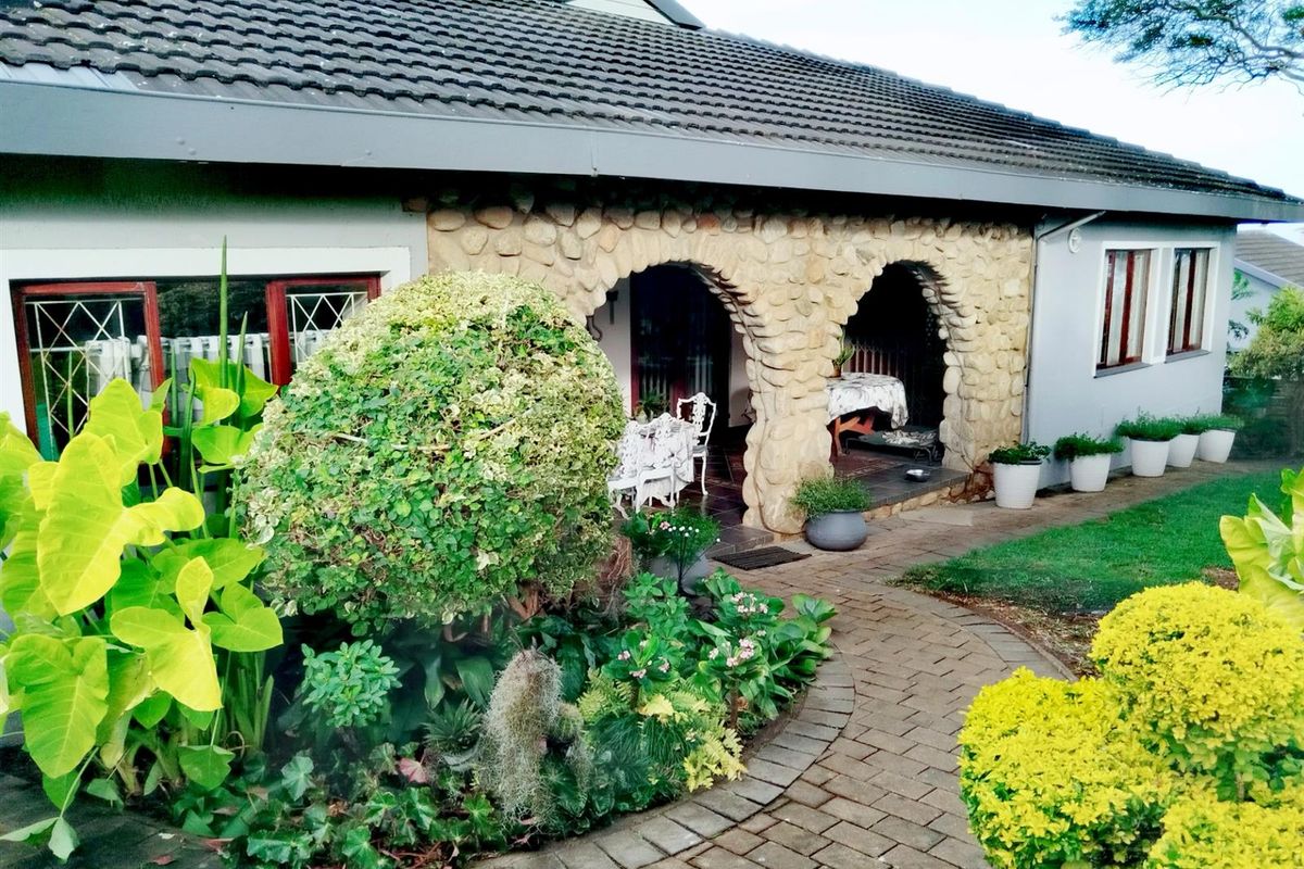 A charming rear exterior view featuring a stone archway leading to a covered patio, complemented by a well-maintained garden and paved walkway.
