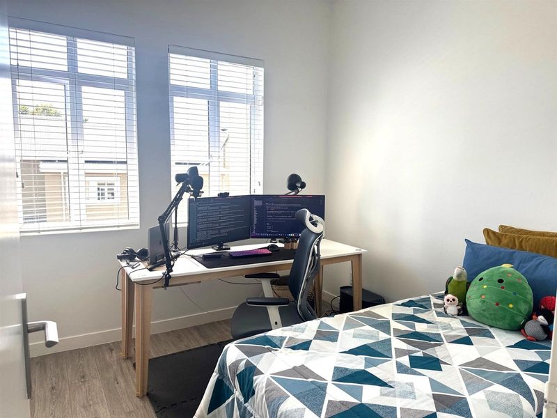 A bright bedroom featuring modern wood-look flooring, neutral walls, and large windows with fitted blinds, providing a comfortable and functional living space.