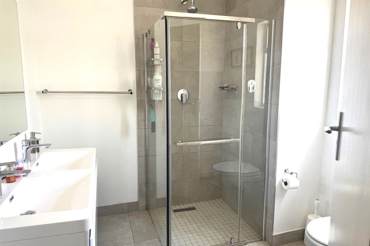 Modern bathroom featuring a glass-enclosed shower, double vanity unit, and neutral floor-to-ceiling tiling.