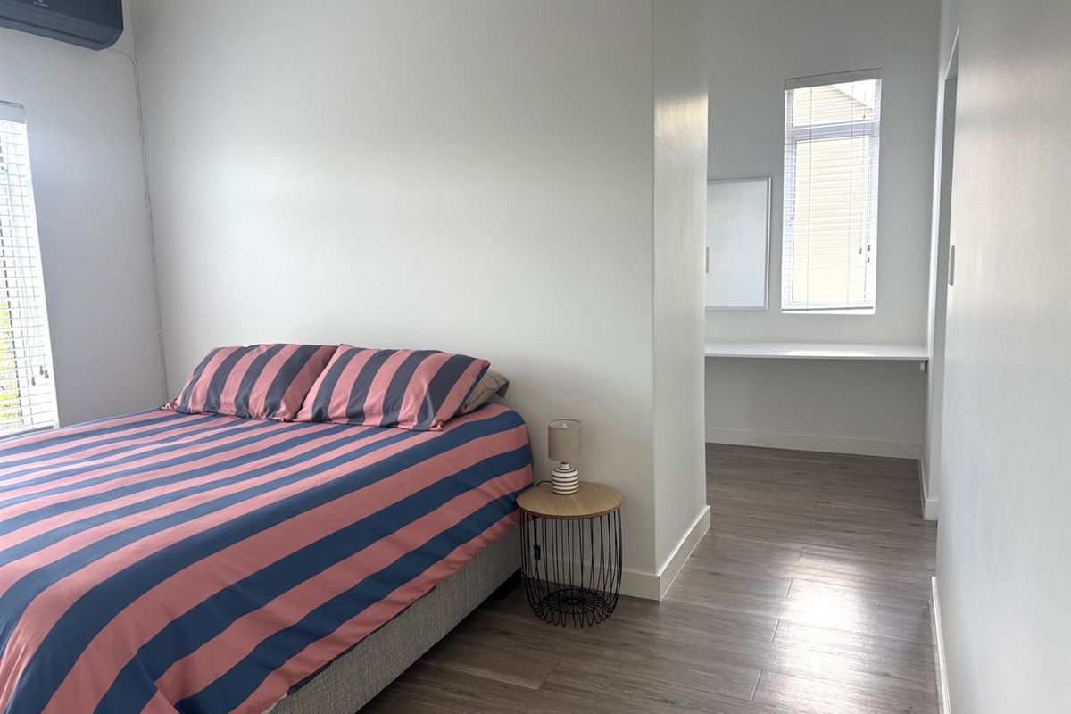 A bright bedroom featuring wood-look flooring, a wall-mounted air conditioning unit, and a built-in desk area in the adjacent alcove.