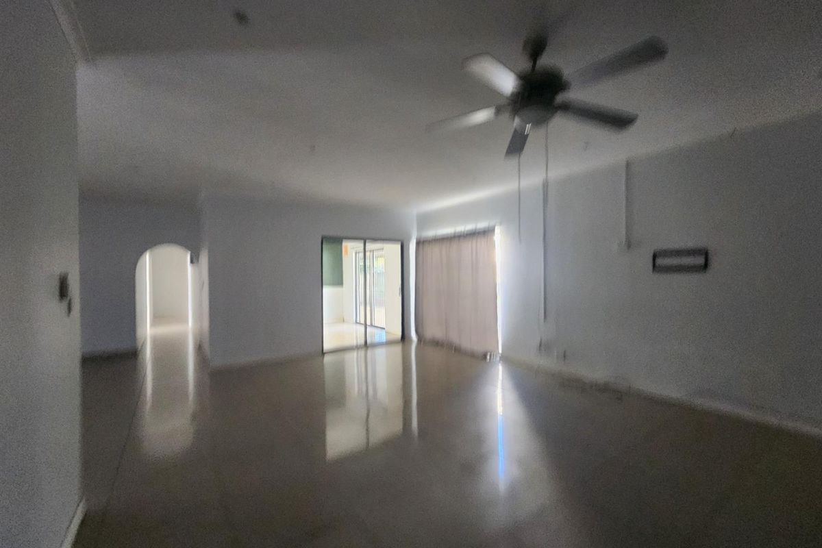 A spacious, empty living room featuring tiled flooring, a ceiling fan, and sliding glass doors leading to an outdoor area.