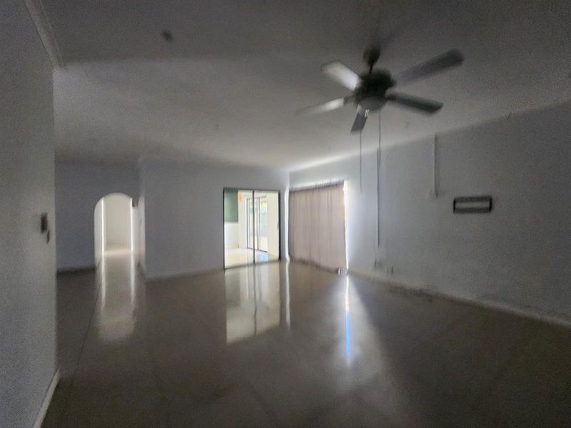 A spacious, empty living room featuring tiled flooring, a ceiling fan, and sliding glass doors leading to an outdoor area.