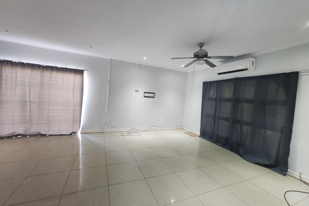 Spacious, empty living area featuring neutral tiled flooring, a ceiling fan, and a wall-mounted air conditioning unit.