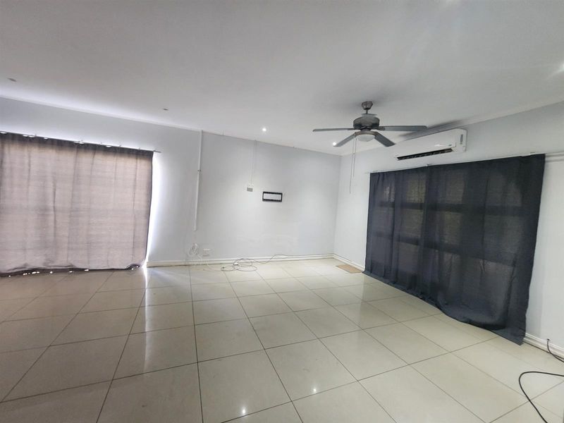 Spacious, empty living area featuring neutral tiled flooring, a ceiling fan, and a wall-mounted air conditioning unit.
