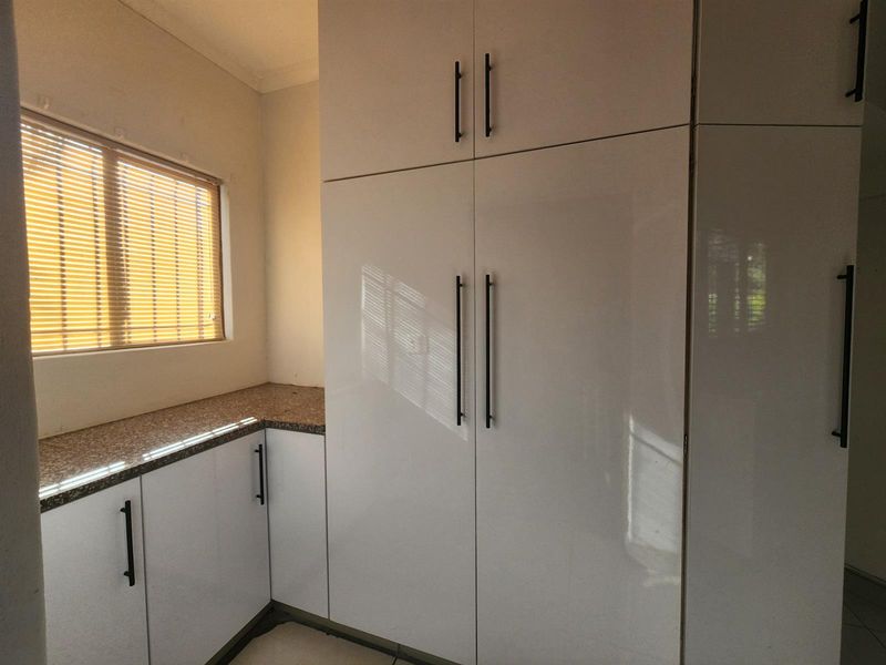 A clean and modern scullery area featuring high-gloss white built-in cabinetry, granite countertops, and natural light through a window with venetian blinds.