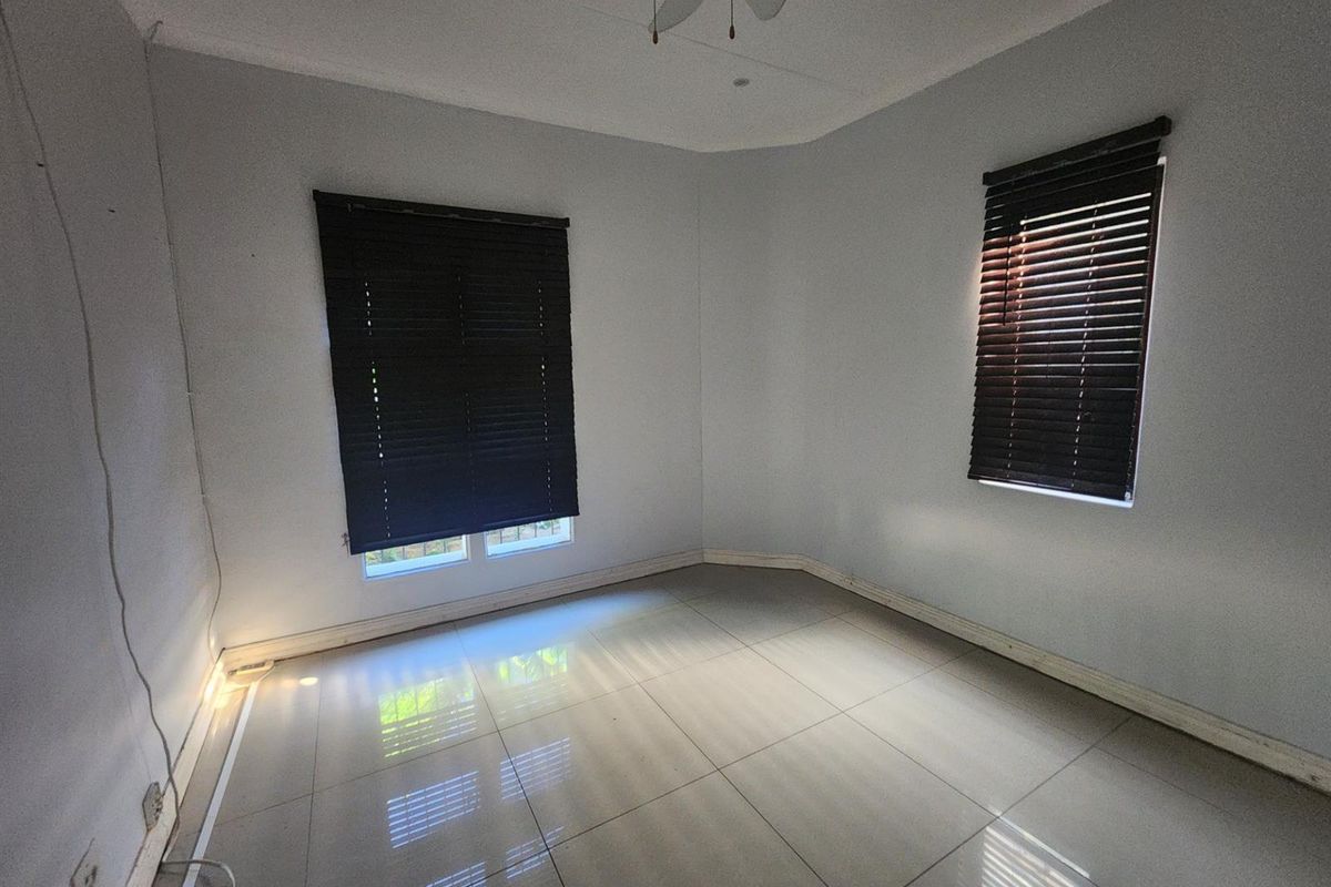 An empty bedroom featuring neutral tiled flooring, a ceiling fan, and dark venetian blinds on the windows.