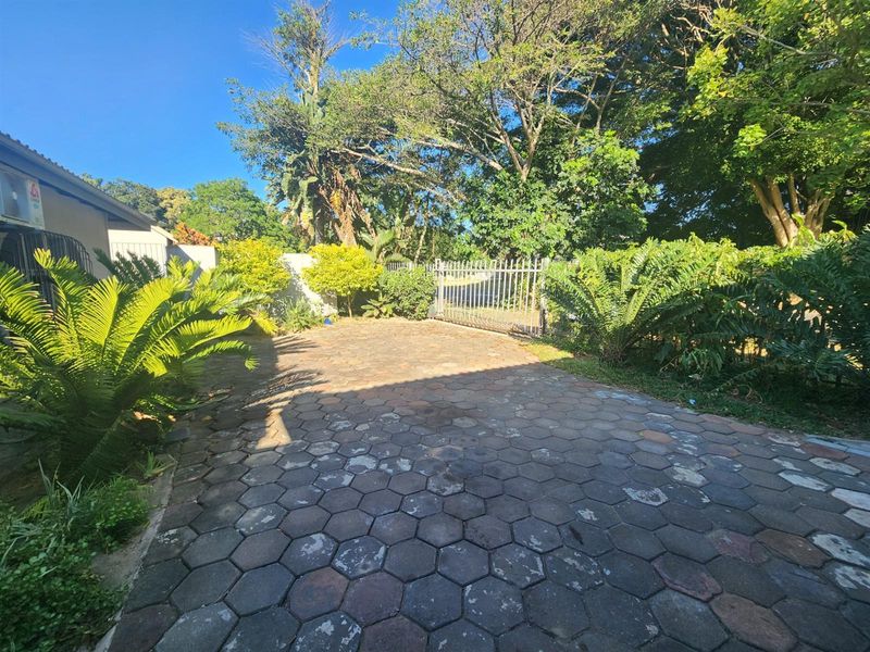 A paved front driveway area featuring a metal security gate and established garden surroundings.