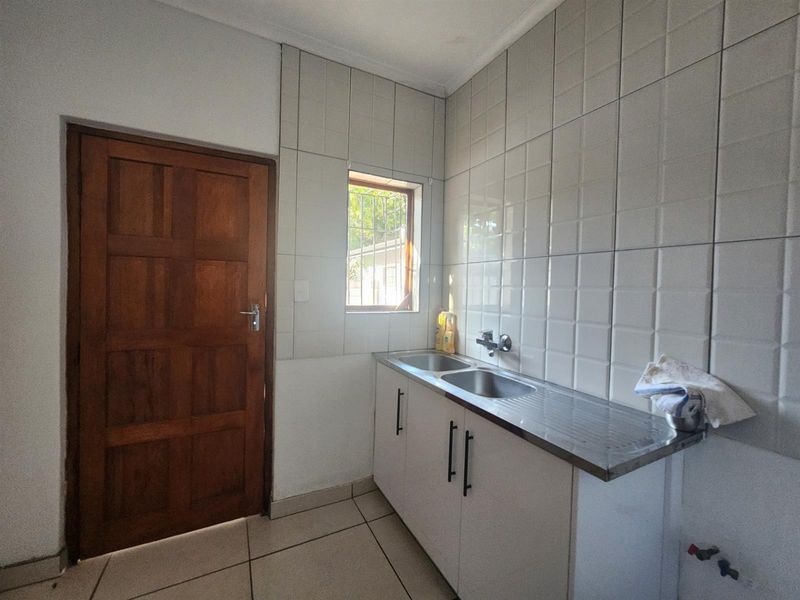 A functional laundry area featuring a stainless steel double sink, tiled splashback, and built-in cabinetry with direct access via a timber door.
