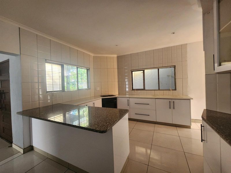 A clean, functional kitchen featuring white cabinetry, granite countertops, tiled backsplash, and tiled flooring with ample natural light from two windows.