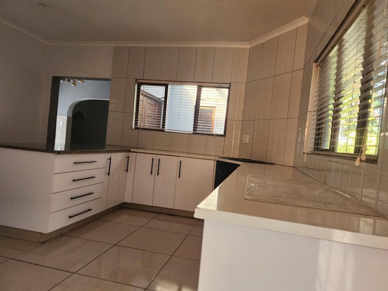 A clean, functional kitchen featuring white cabinetry, stone countertops, tiled backsplash, and tiled flooring, offering a bright and neutral space for culinary activities.