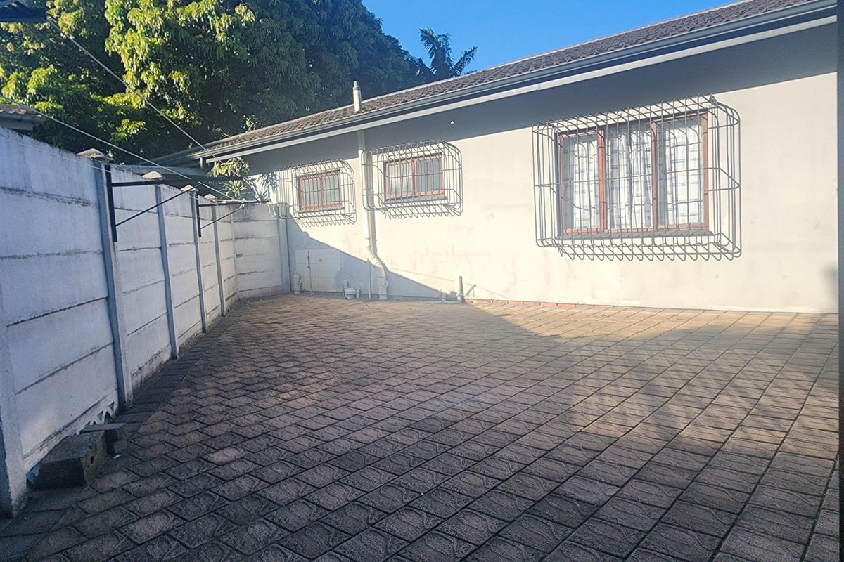 A paved rear courtyard area featuring a precast concrete boundary wall and windows fitted with security bars.